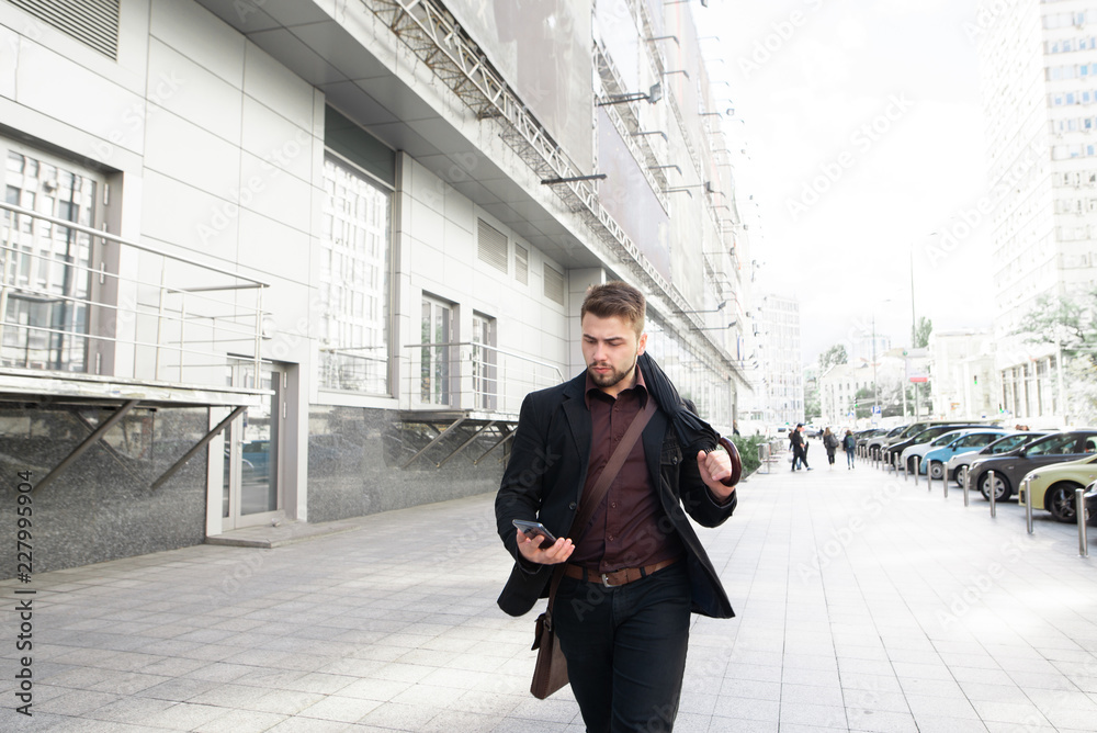 Portrait of a business man walking down the street with an umbrella in his hands on an autumn day and using a smartphone.Against the background of the urban landscape Portrait of a business man walking down the street with an umbrella in his hands on an autumn day and using a smartphone.Against the background of the urban landscape