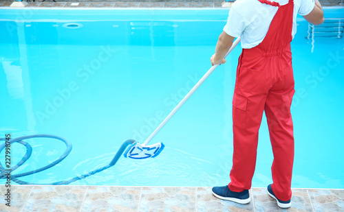 Male worker cleaning outdoor pool with underwater vacuum