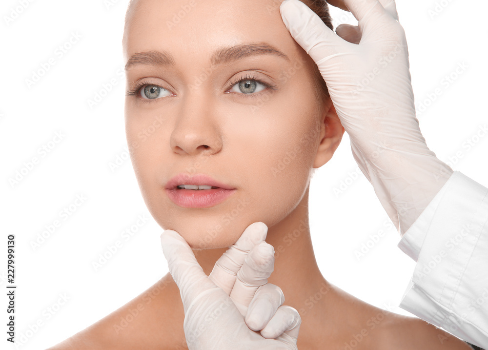 Doctor examining young woman face before cosmetic surgery on white background