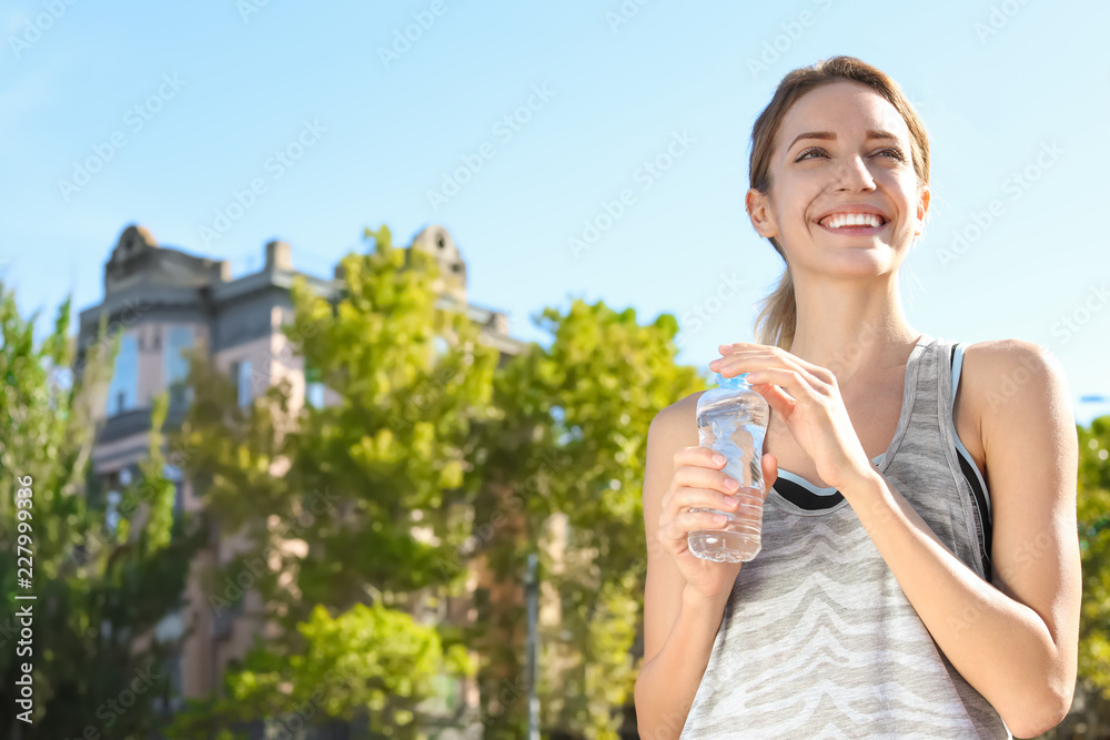 Young woman holding bottle with clean water on street. Space for text Young woman holding bottle with clean water on street. Space for text