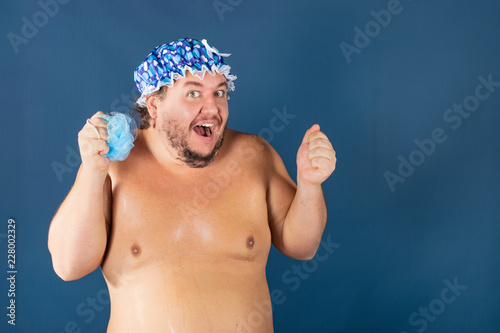 Funny fat man in blue cap and with sponge in the shower