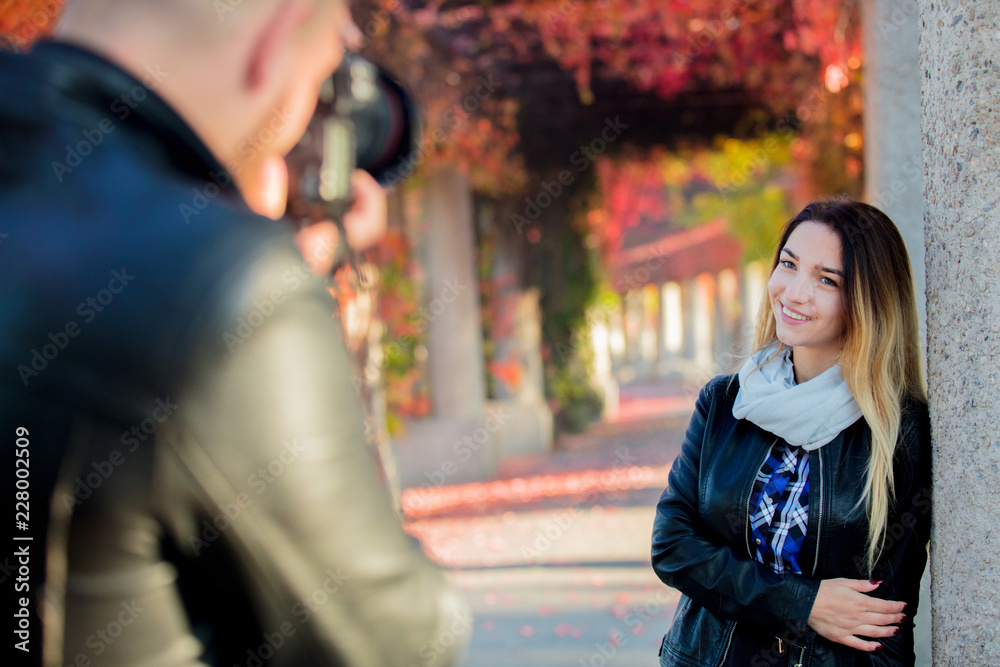 Young photographer making a photo of a beautiful girl in a park. Autumn season time
