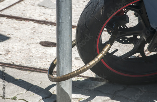 Rear wheel of powerful motorcycle locked with chain bike lock to road sign pole closeup in sunny day