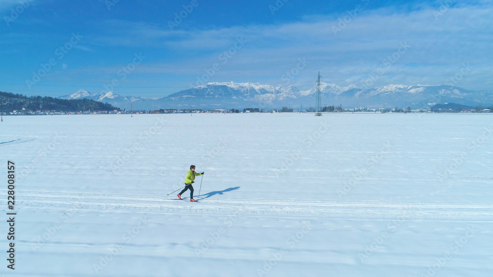 Naklejka premium AERIAL: Flying along an active woman skiing across vast snowy plain in Slovenia.
