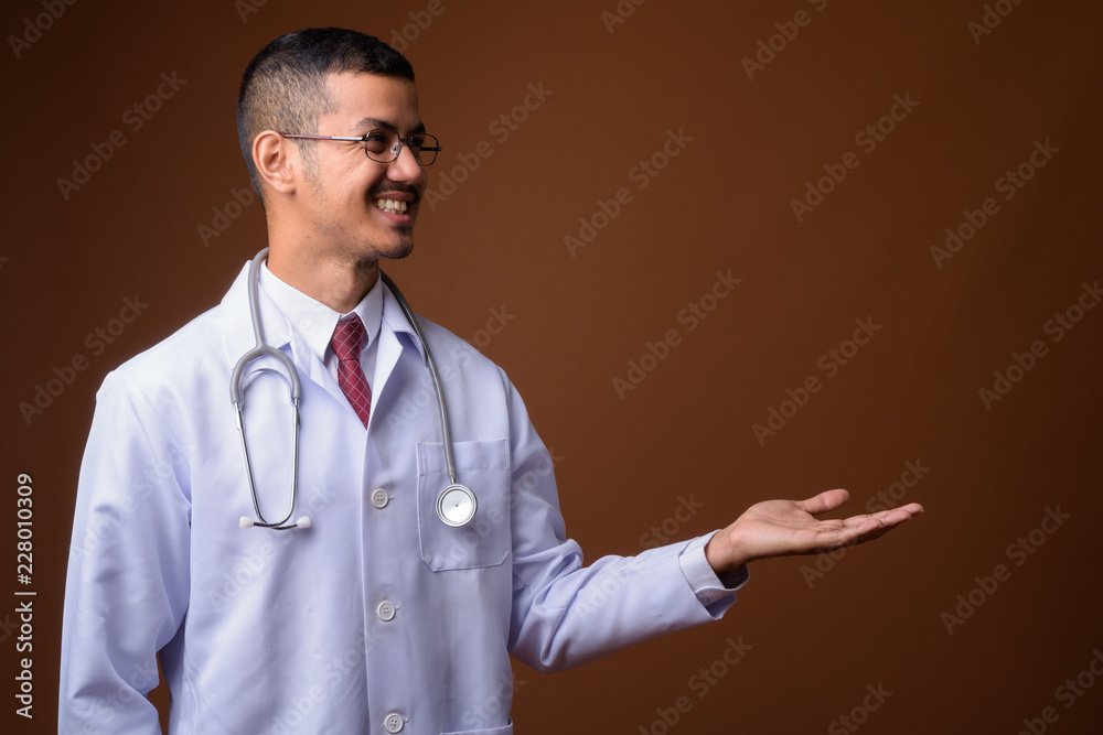 Young multi-ethnic Asian man doctor against brown background Young multi-ethnic Asian man doctor against brown background