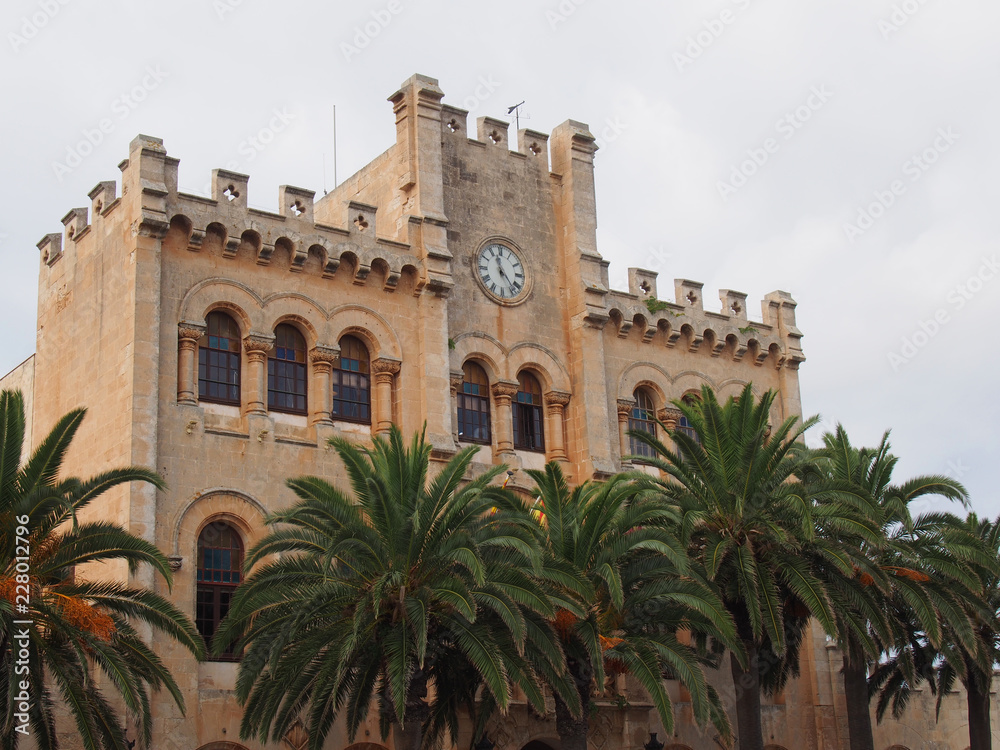 view of the historic town hall in ciutadella menorca surrounded by palm trees and blue sunlit summer sky
