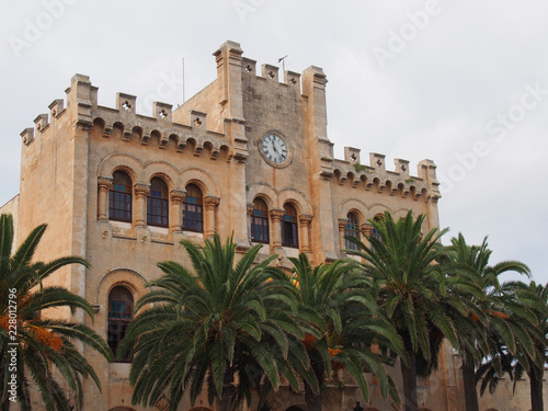 view of the historic town hall in ciutadella menorca surrounded by palm trees and blue sunlit summer sky