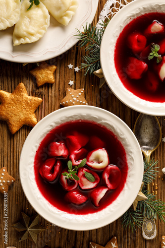 Christmas beetroot soup, borscht with small dumplings with mushroom filling in a ceramic bowl on a wooden table, top view.  Traditional Christmas eve dish in Poland. 