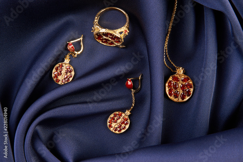 Rubies ring, necklace and earrings on blue silk background with copy space. Beautiful precious women's gold jewelry, close-up. 