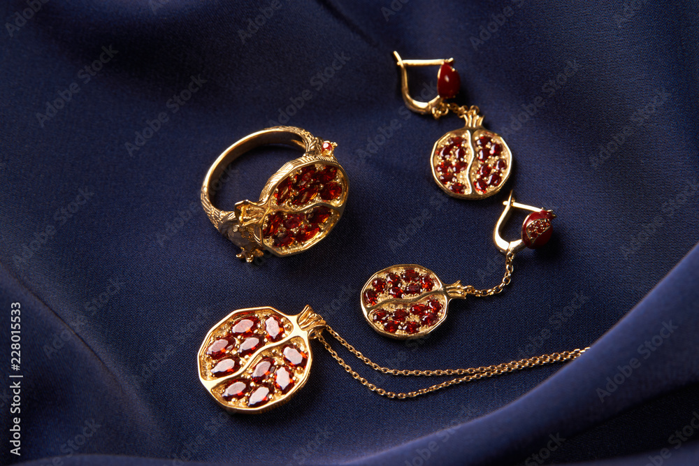 Rubies ring, necklace and earrings on blue silk background with copy space. Beautiful precious women's gold jewelry, close-up. Rubies ring, necklace and earrings on blue silk background with copy space. Beautiful precious women's gold jewelry, close-up.