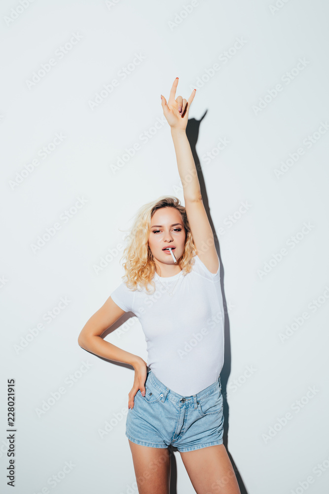 Hipster blonde girl in white t-shirt smoking cigarette and giving the Rock  and Roll sign isolated on white background Stock Photo | Adobe Stock