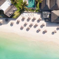 Aerial view of beautiful tropical beach front hotel resort with swimming pool, palm leaves umbrellas and turquoise sea. Paradise destination for vacations in Mauritius.