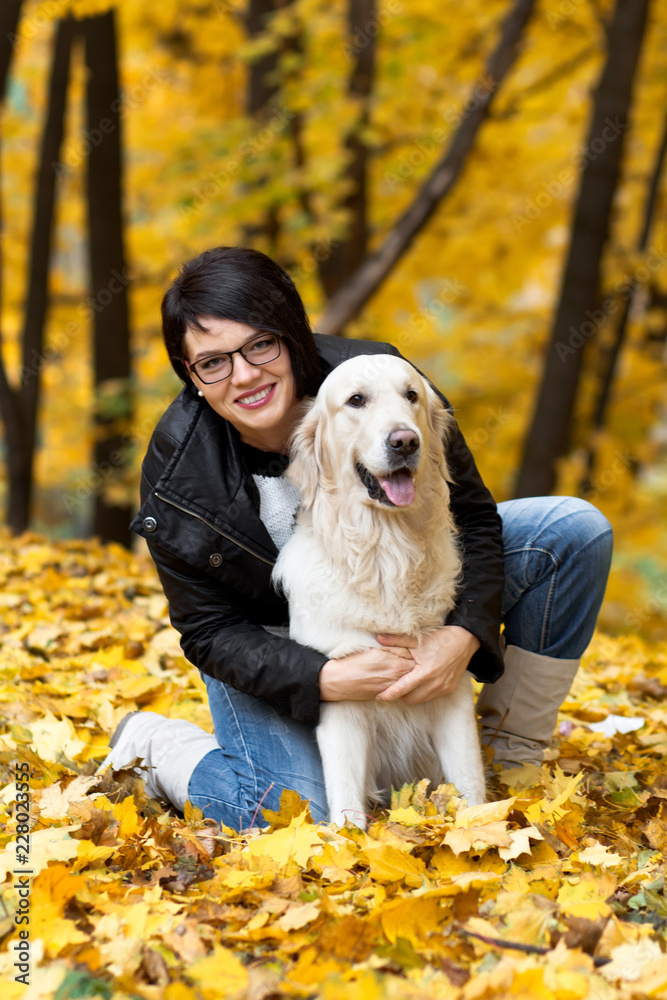 Happy woman hugs her dog in autumn park.