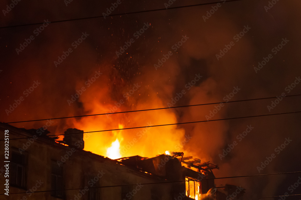 Burning building at night, roof of house in fire flames