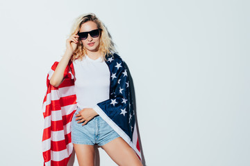 Young and carefree. Beautiful young blonde woman carrying American flag and smiling while celebrate 4th of July, Independence day standing against white background