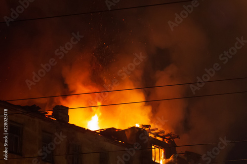 Burning building at night, roof of house in fire flames