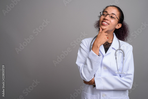 Young beautiful African woman doctor against gray background