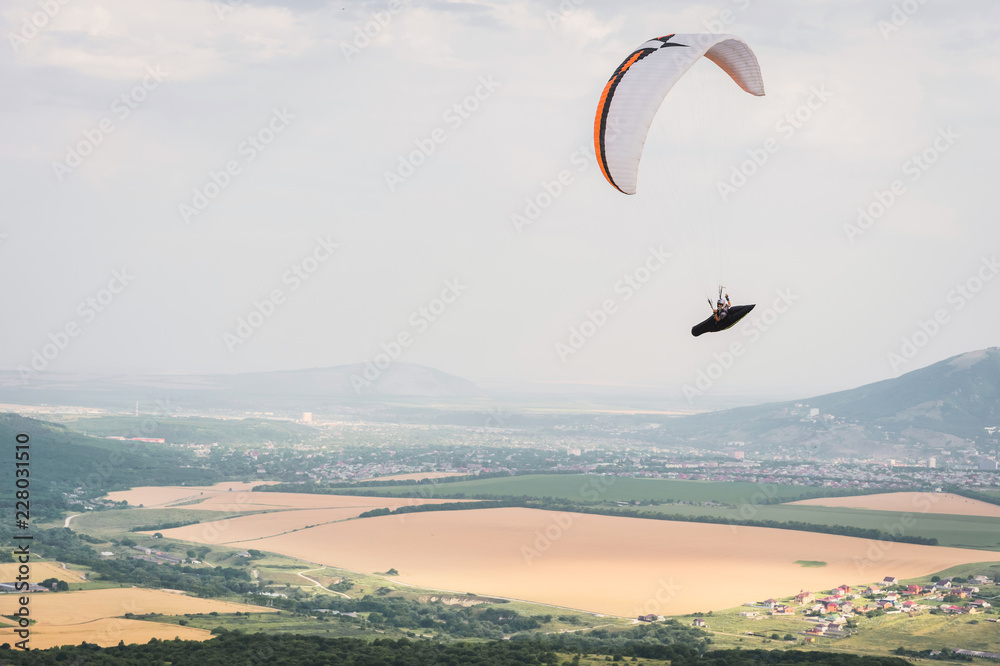 A white-orange paraglider flies over the mountainous terrain A white-orange paraglider flies over the mountainous terrain