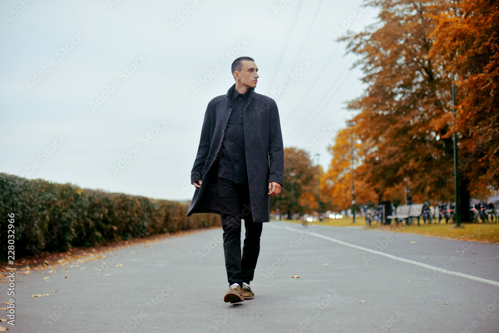 Young handsome man in coat. Fashionable well dressed man posing in stylish coat. Confident and focused boy outdoor at autumn. Elegant man with perfect hairstyle. Man walks in the park.