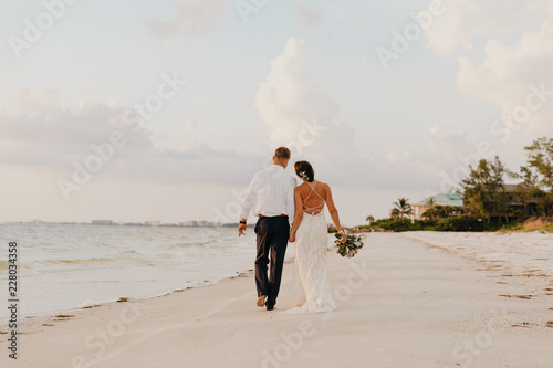 Fototapeta Naklejka Na Ścianę i Meble -  Perfect Sunset Destination Beach Wedding with Beautiful Bride and Groom Walking Down the Coastline