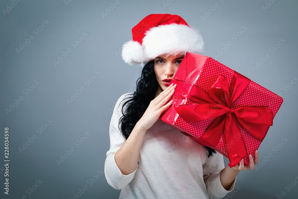 Young woman with santa hat holding a gift box on a gray background Young woman with santa hat holding a gift box on a gray background