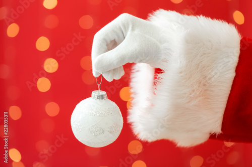 Santa holding a Christmas bauble on a shiny light red background