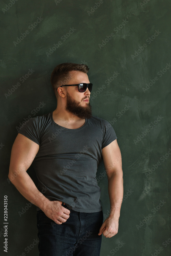 Bodybuilder in sunglasses portrait. Muscular man with a beard in a tight t-shirt looks to the side.