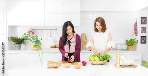 Beautiful Asian girl in casual dress is order fake fruit into wooden basket smile happily in a modern white kitchen.