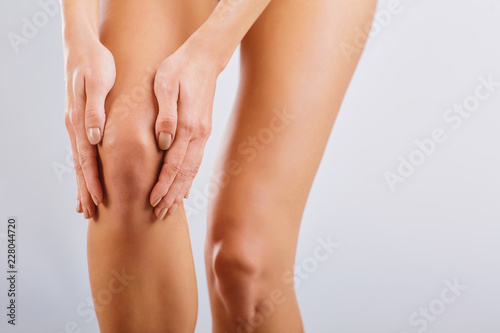 Pain, injury to the knee. A woman holds her knee with her hand.
