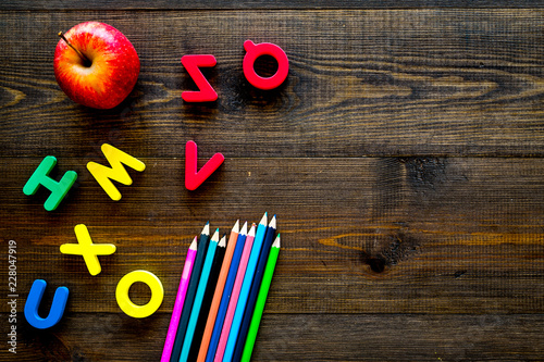 Elemerntary school concept. Letters of toy alphabet, apple and color pencils on dark wooden background top view copy space