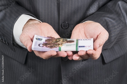 bundle of money in denominations of five hundred euros and eurocents on it in the hands of a businessman in a suit photo