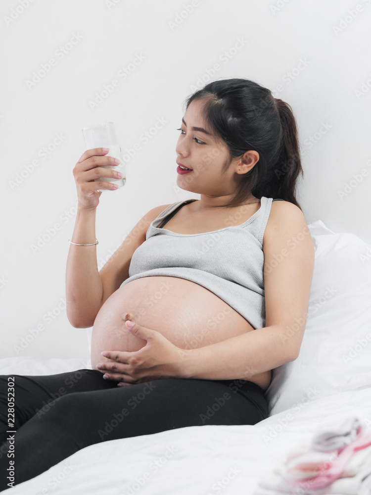 Asian pregnant woman drinking a glass of milk at sitting on bed at home, lifestyle concept. Asian pregnant woman drinking a glass of milk at sitting on bed at home, lifestyle concept.