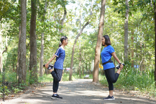 Asian mother and daughter warm up stretch thigh muscles before running at the park