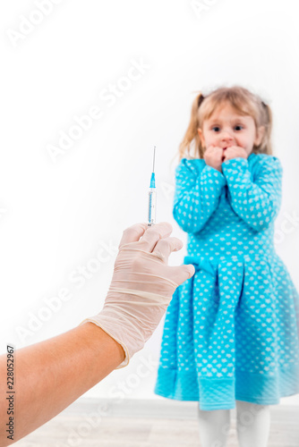 Doctor holds syringe to vaccinate sick baby with injection. Crying and fear a little patient before the injection.