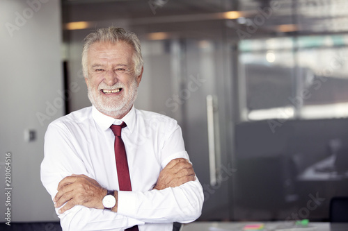 Happy handsome old businessman standing and smiling in office