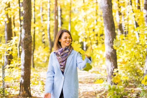 Autumn, nature and fun concept - Young beautiful woman in blue coat throwing bouquet of leaves