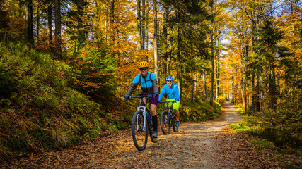 Cycling, mountain biker couple on cycle trail in autumn forest. Mountain biking in autumn landscape forest. Man and woman cycling MTB flow uphill trail.