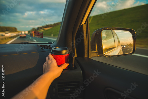 hand taking cup from cup holder in car. sunset reflection in car mirror on highway photo
