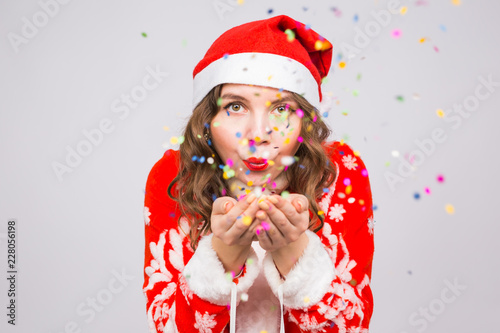 Christmas, people concept - woman in santa suit blowing colourful sequins on background with copy space © satura_