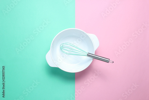 White empty bowl with a whisk on a pastel colored background. Top view, minimalism.