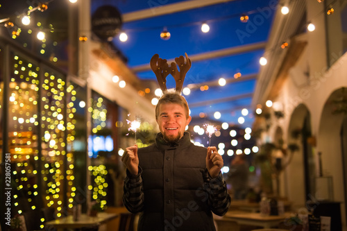 People, holidays and Christmas concept - young funny man in christmas deer costume with bengals light outdoors © satura_