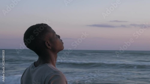 prayer, faith, God. Young african man on the beach praying looking at the sky