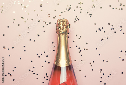 Christmas or New Year pink background with bottle of sparkling wine, rose champagne and gold decor, top view
