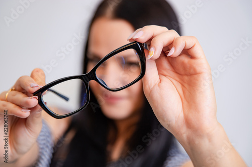 woman holds and shows eyeglasses with black rim on a white background. Close-up