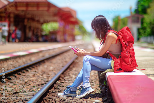 asian young woman checking train schedule online by mobile phone, or chating social online during waiting for the next train, waste time activity in trip waiting photo