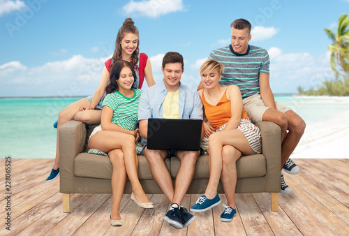 travel, tourism and technology concept - group of happy smiling friends with laptop computer sitting on sofa over tropical beach background in french polynesia