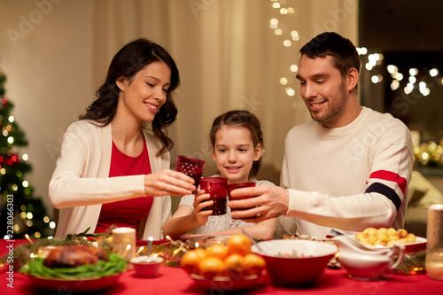 holidays, family and celebration concept - happy mother, father and little daughter with drinks toasting at home christmas dinner