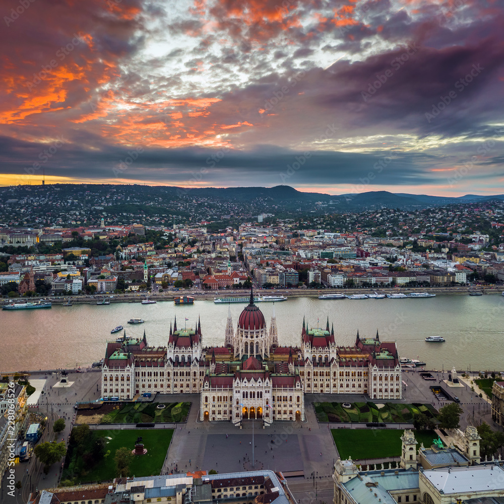 Fototapeta premium Budapest, Hungary - Aerial panoramic view of the Parliament of Hungary at sunset with sightseeing boats on River Danube and beautiful dramatic purple clouds