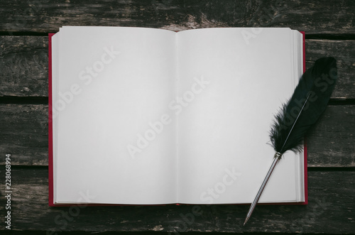 Open book with empty blank pages and feather pen on the table.