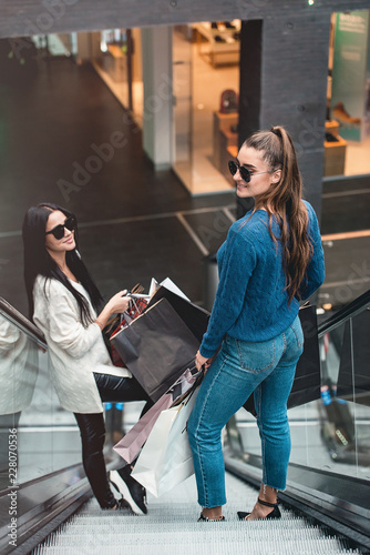 Beautiful girls with paper bags on escalator at supermarket